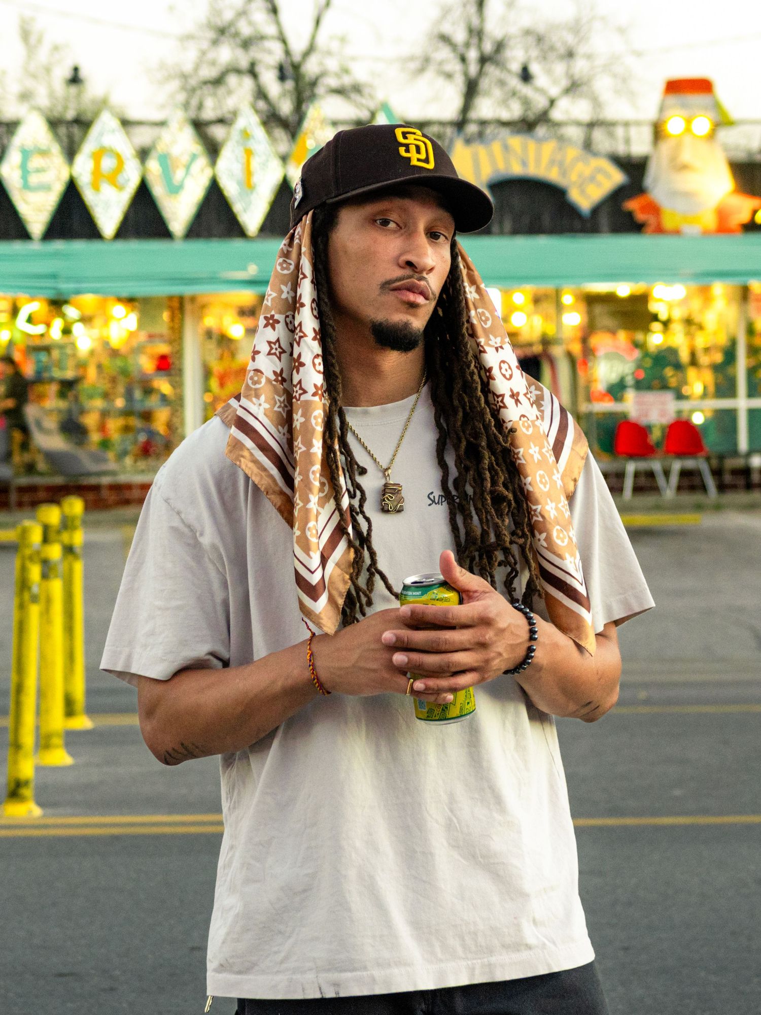 Candid portrait of a man in an SD Padres cap and bandana holding a drink at a colorful amusement park in Austin.