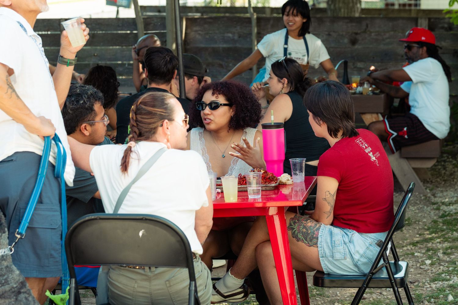 Group of friends socializing at a red outdoor table during a sunny community event.