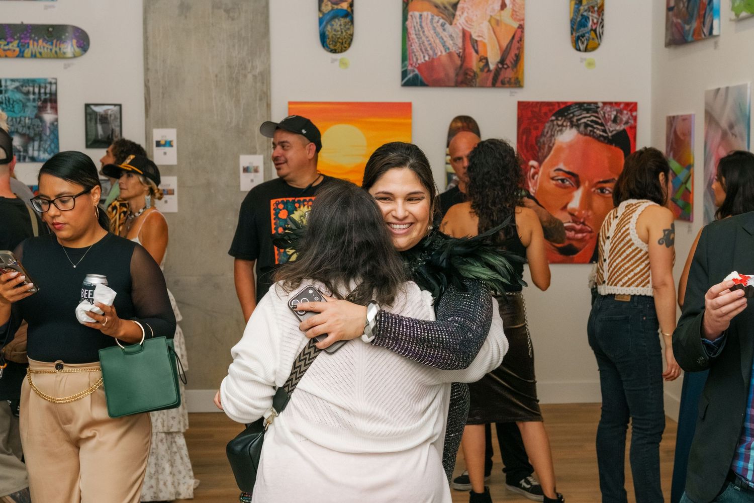 People hugging and socializing at a lively art gallery opening with colorful paintings.
