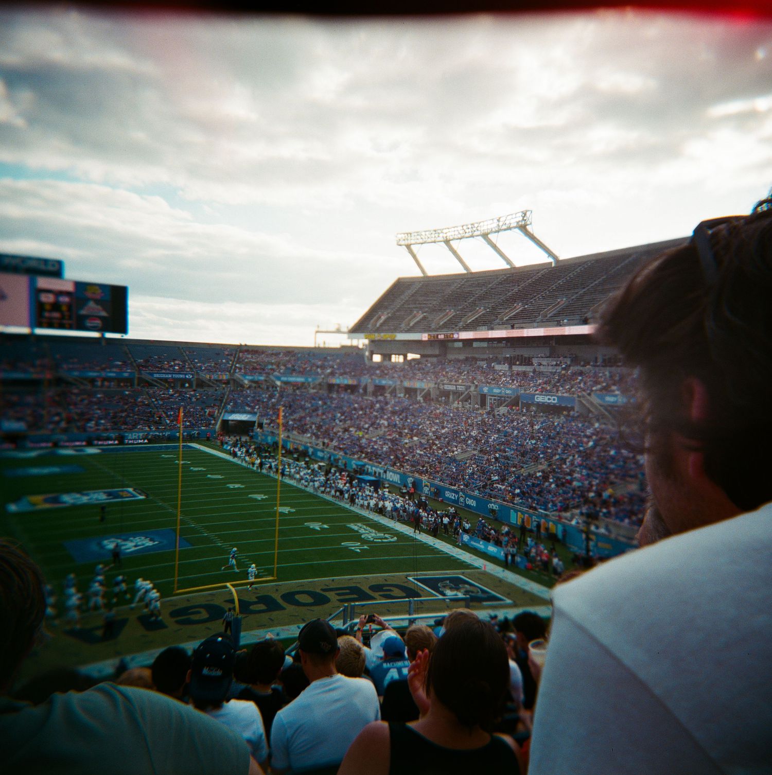 Aerial view of a packed football stadium with green field and cloudy sky from upper deck seats.