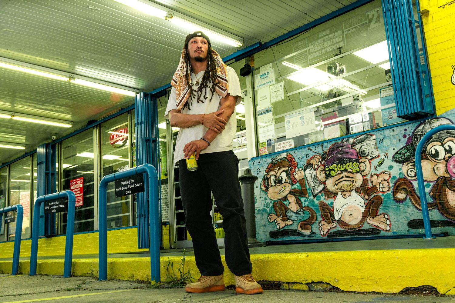 Documentary-style portrait of a man with dreadlocks before a vibrant graffiti mural at an urban corner store, Austin street photography.