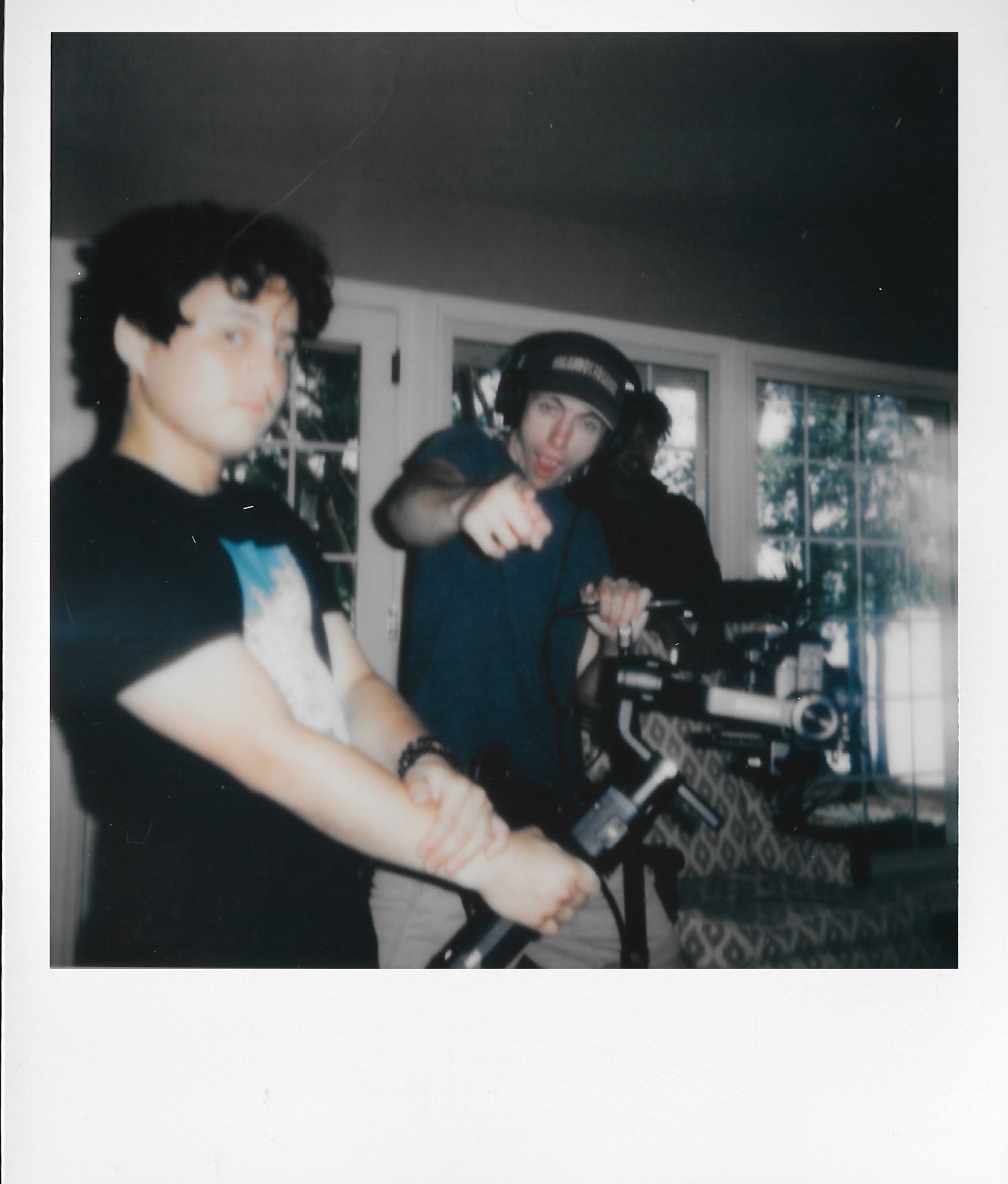 Two filmmakers operating a camera on a gimbal stabilizer indoors, one pointing direction during a video production shoot.