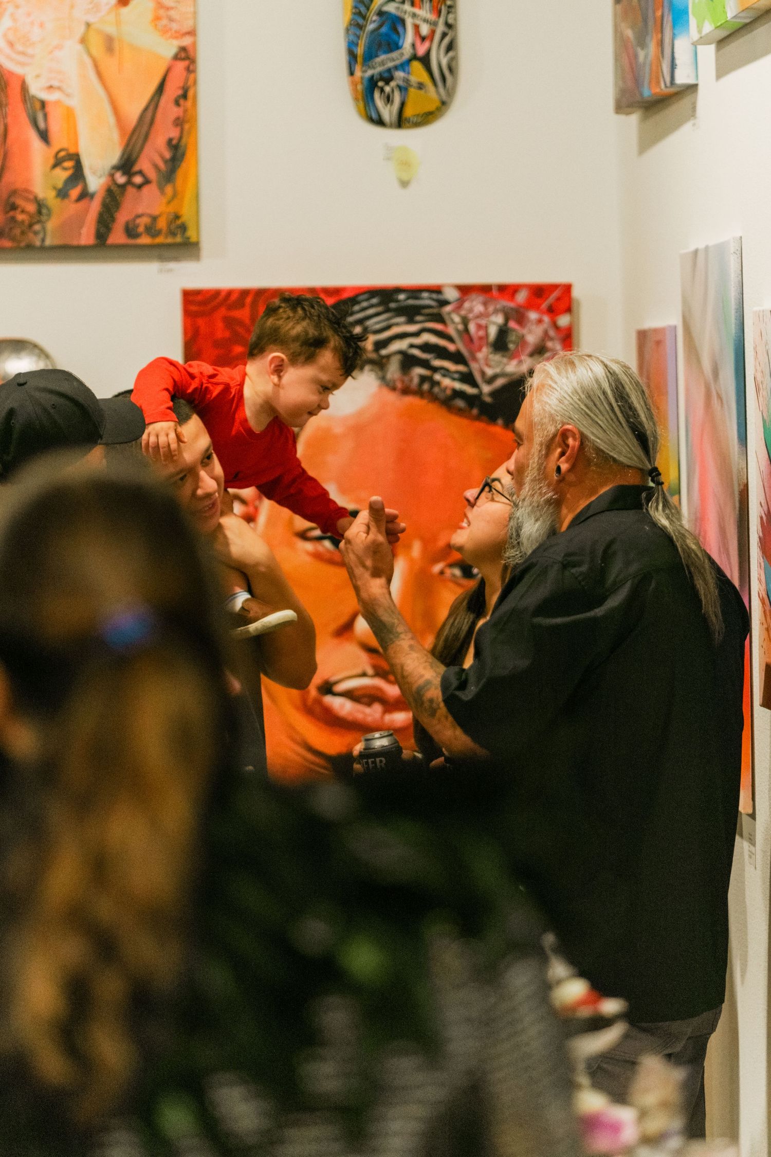 Child leaning down from shoulders interacting with older man near large portrait painting at art gallery.