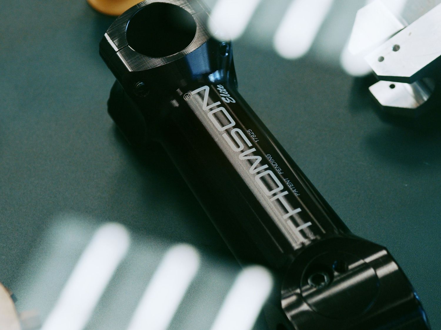 Black anodized aluminum bicycle stem with Thomson branding on dark surface with light streaks.