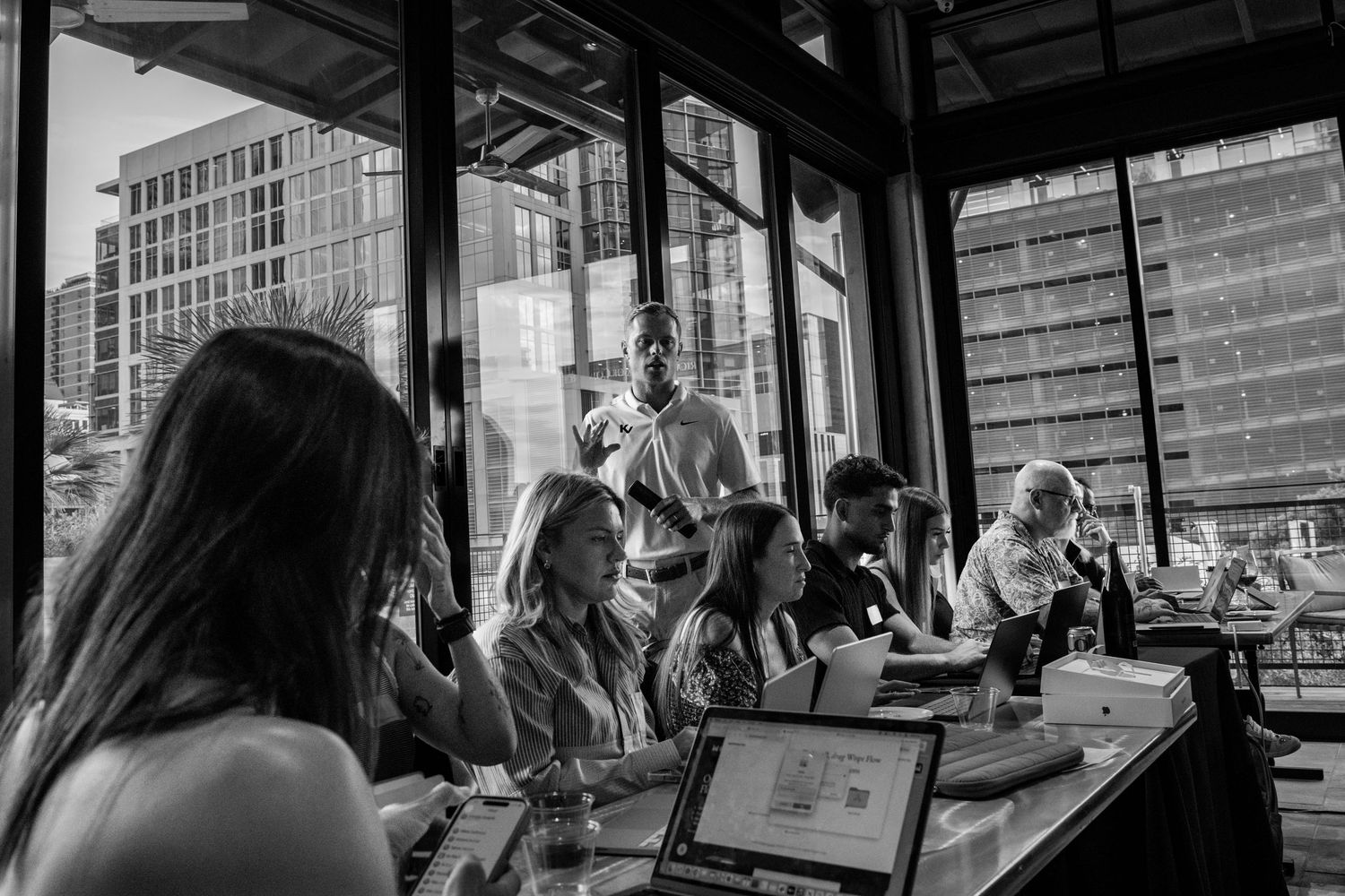 Black and white photo of people dining at a modern restaurant with large windows overlooking a city skyline.
