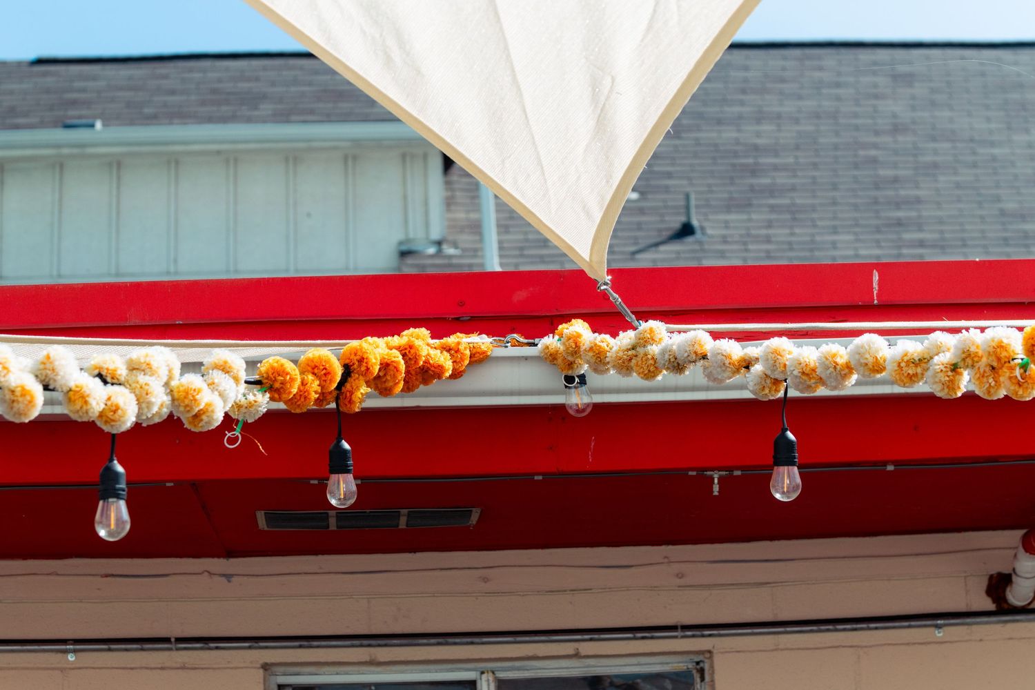 Red awning decorated with orange and yellow floral garland and hanging Edison bulb lights.
