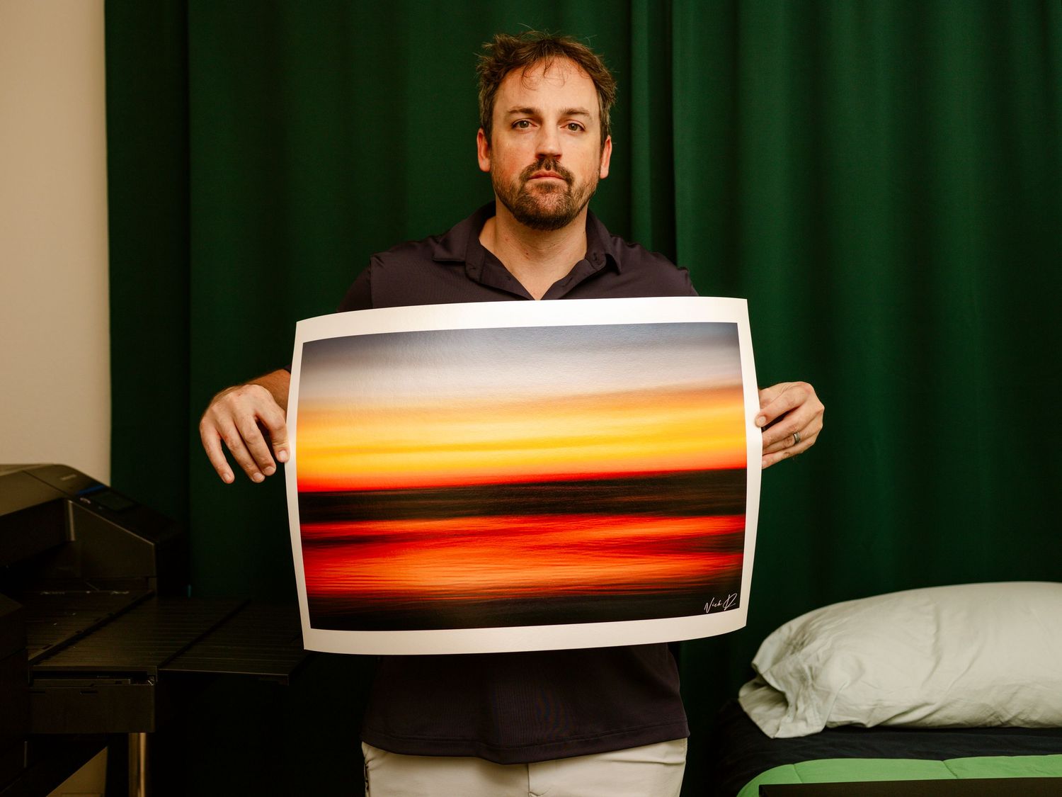 Photographer holding a large fine art abstract sunset print in front of green curtains.