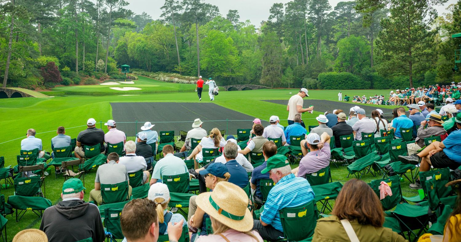Crowds watch golfers on a lush green Masters Tournament course at Augusta National Golf Club.