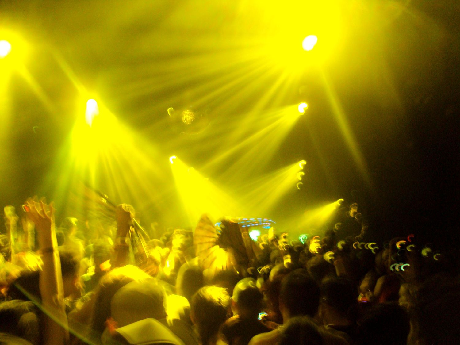 Crowd of concert-goers bathed in yellow stage lights at a live music event.