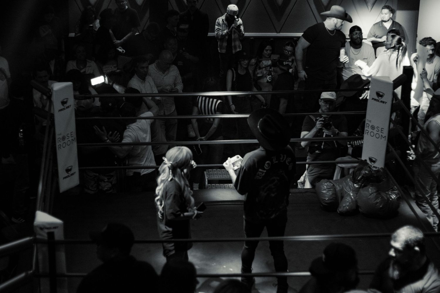 Black and white aerial view of a blonde woman standing in a boxing ring at a live event.