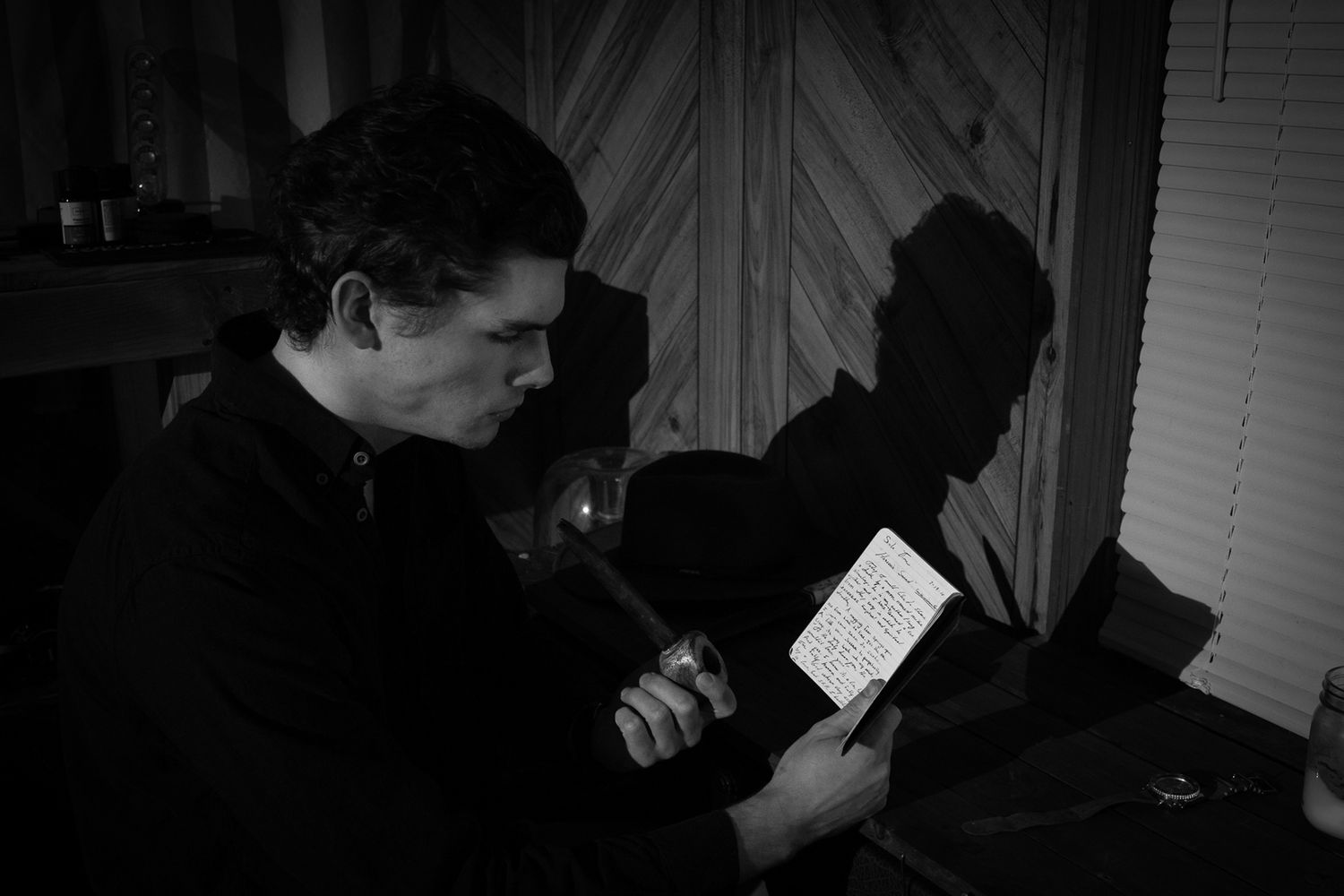Black and white photo of a man reading illuminated papers in a dimly lit room at night.