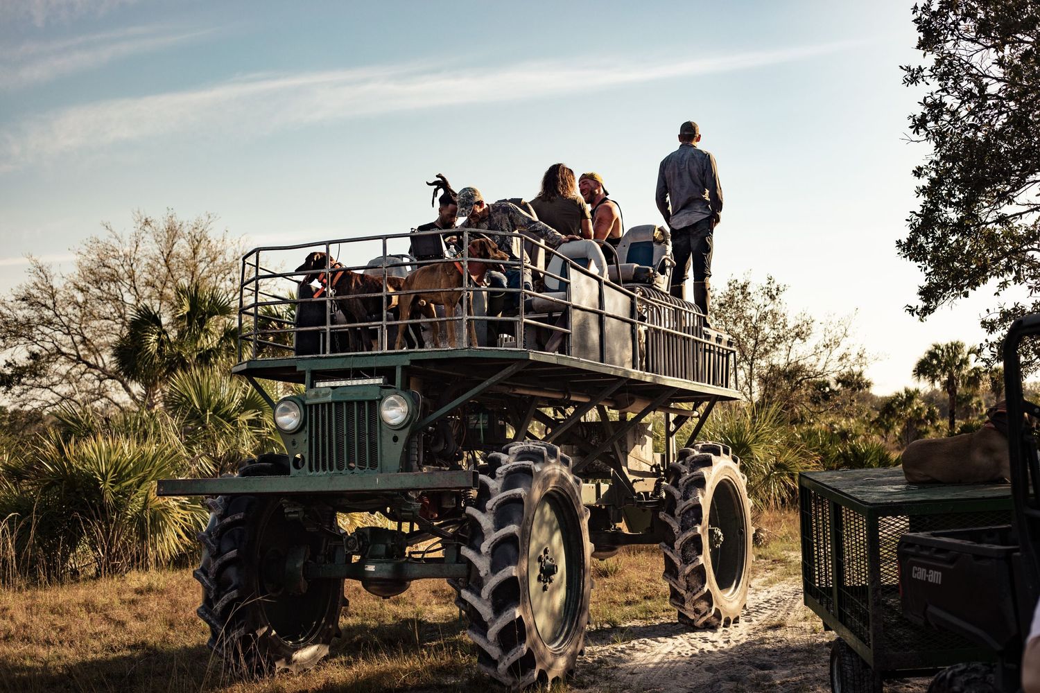 Group of tourists standing on a large monster truck safari vehicle in a Florida nature preserve at dusk.