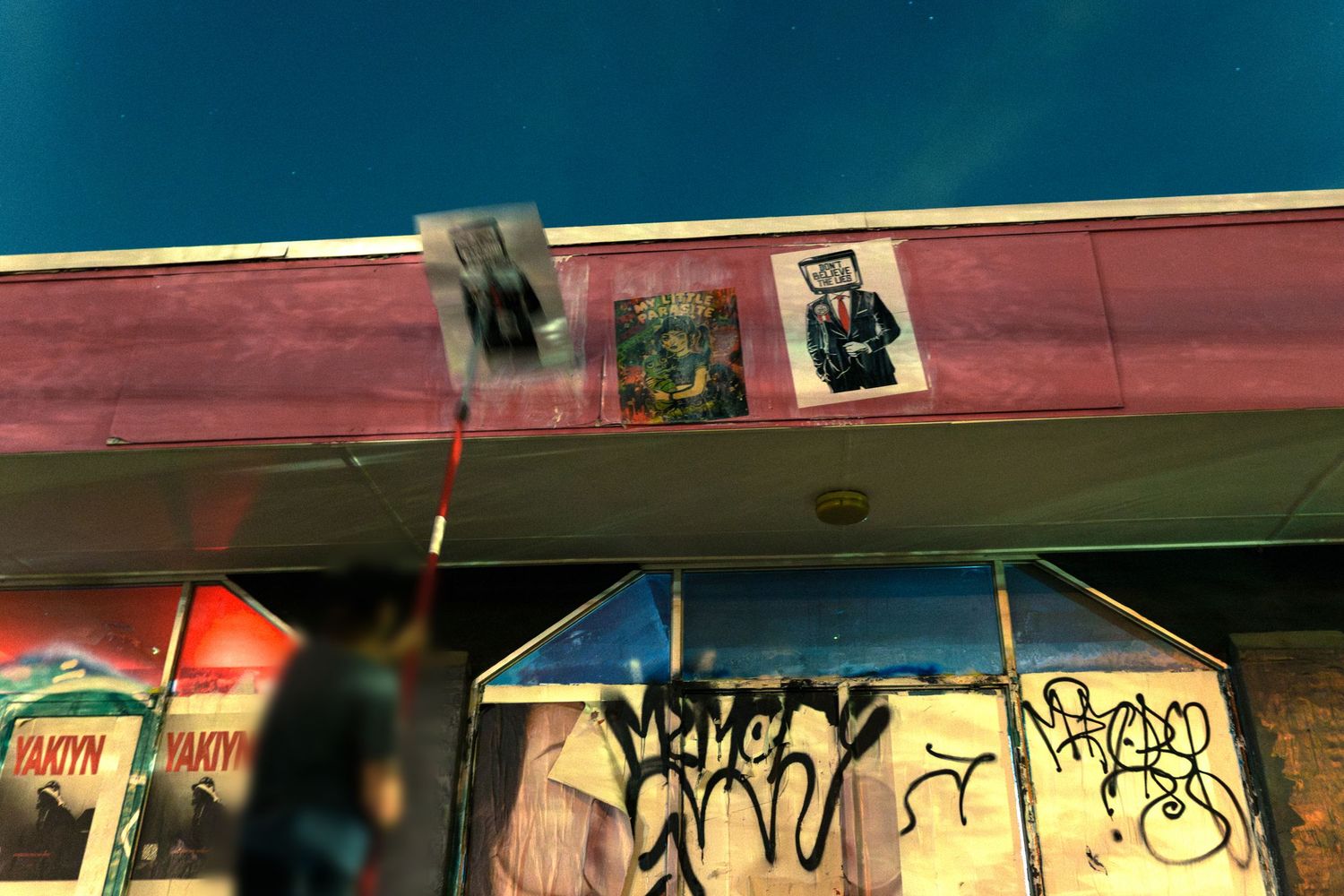 Urban building exterior with graffiti-covered walls, colorful street art posters, and a person standing near the entrance.