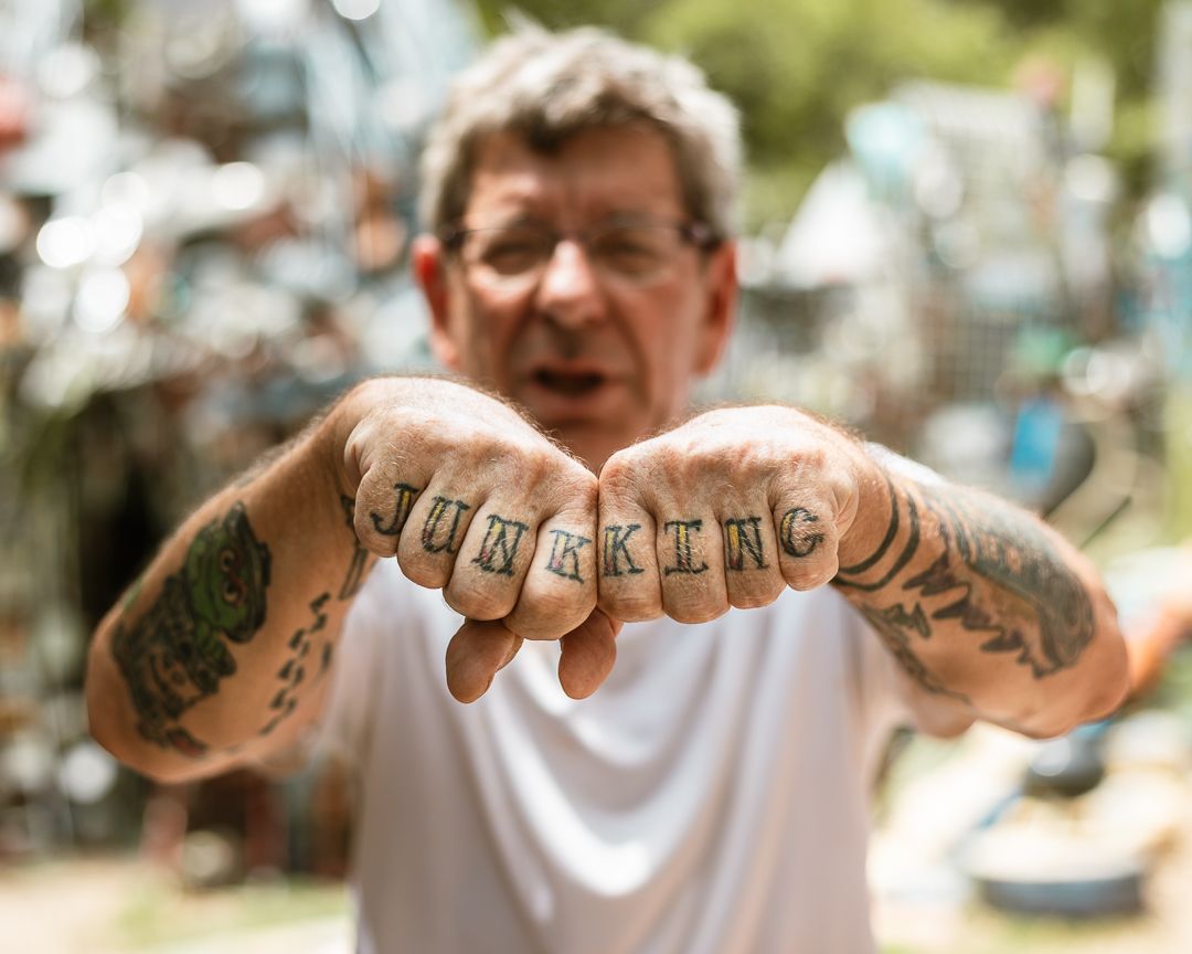 Man with knuckle tattoos spelling JUNKING shows fists covered in tattoo sleeves outdoors.