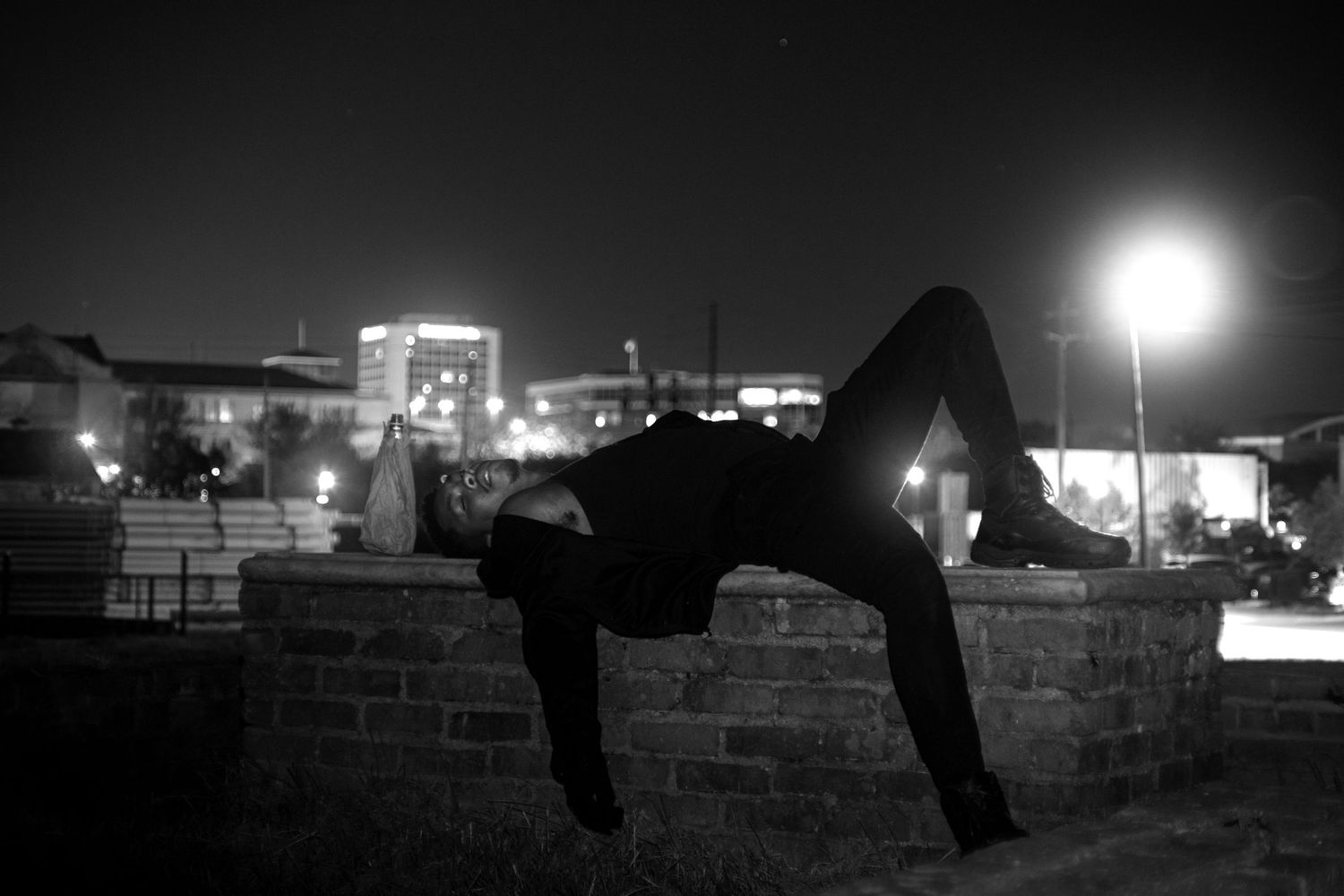 Person performing a backbend on a brick wall at night with city lights in the background.