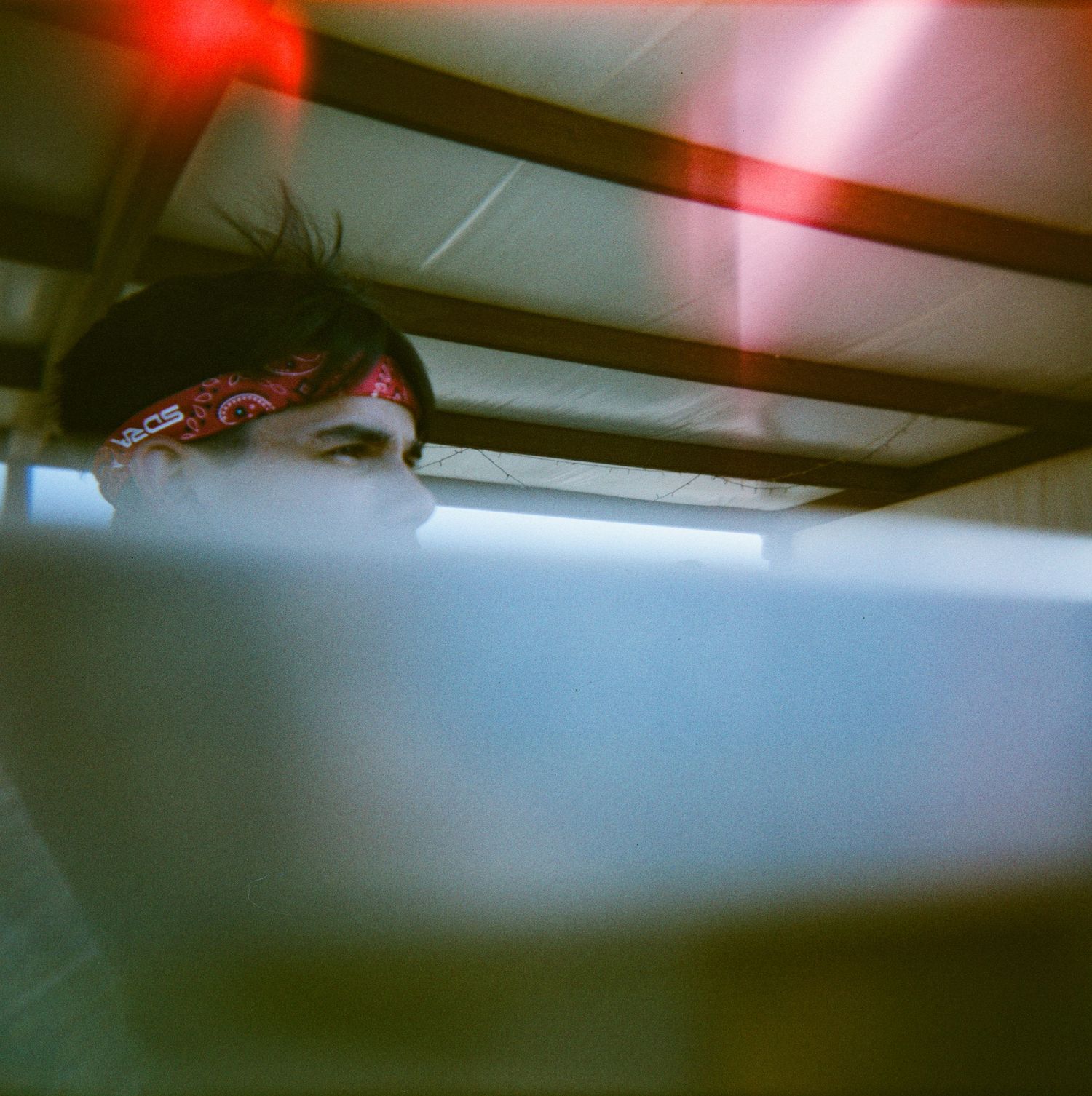 Person wearing red bandana headband working at computer in dimly lit room with red light overhead.
