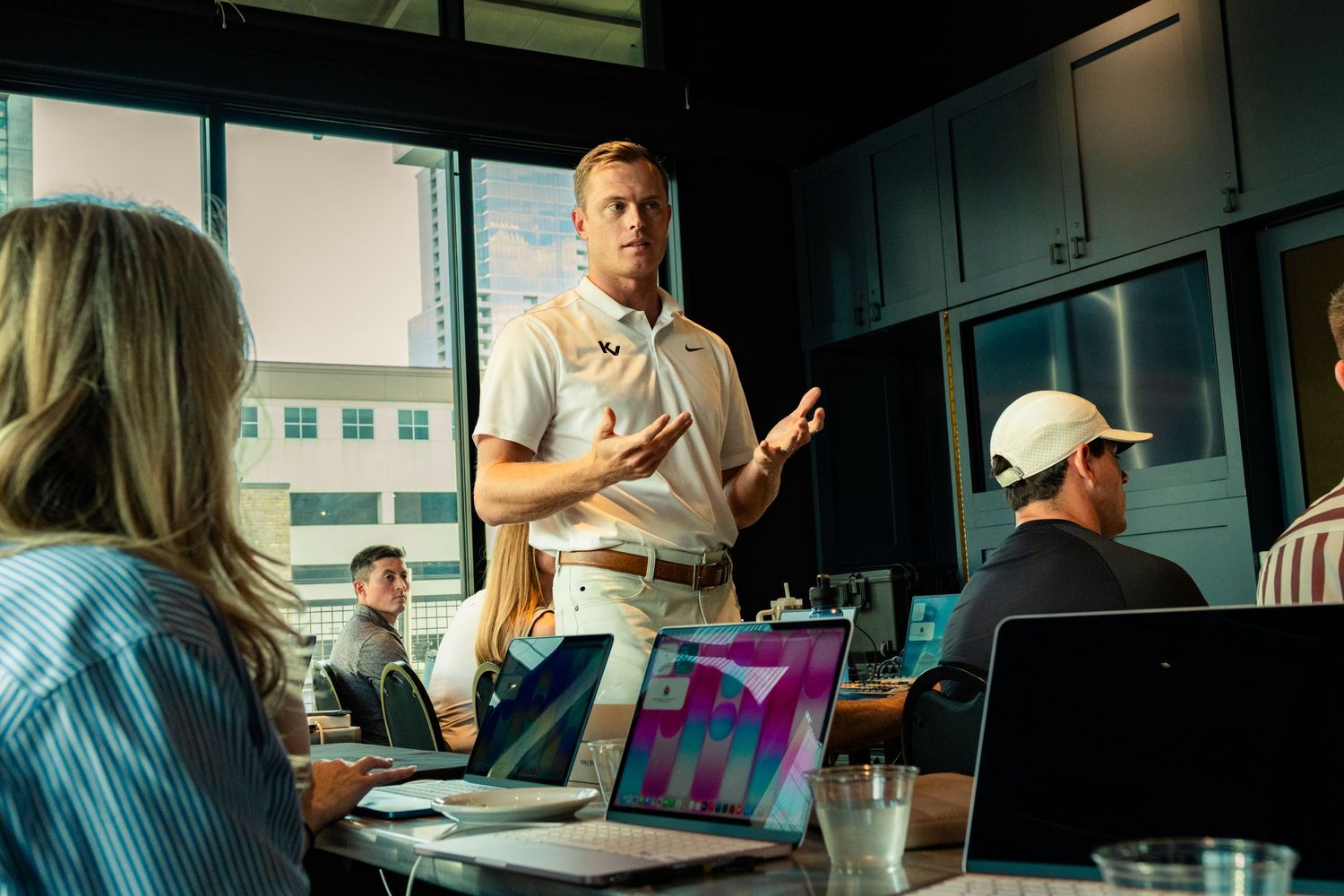 Professional man presenting to colleagues in a modern office meeting room with laptops on the table.