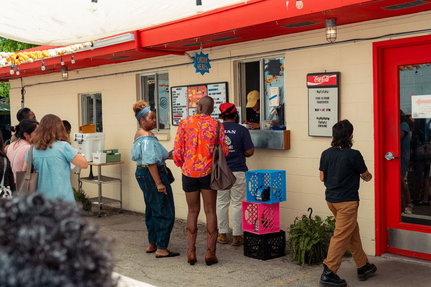 Customers lining up outside a small colorful food stand at an outdoor community event.