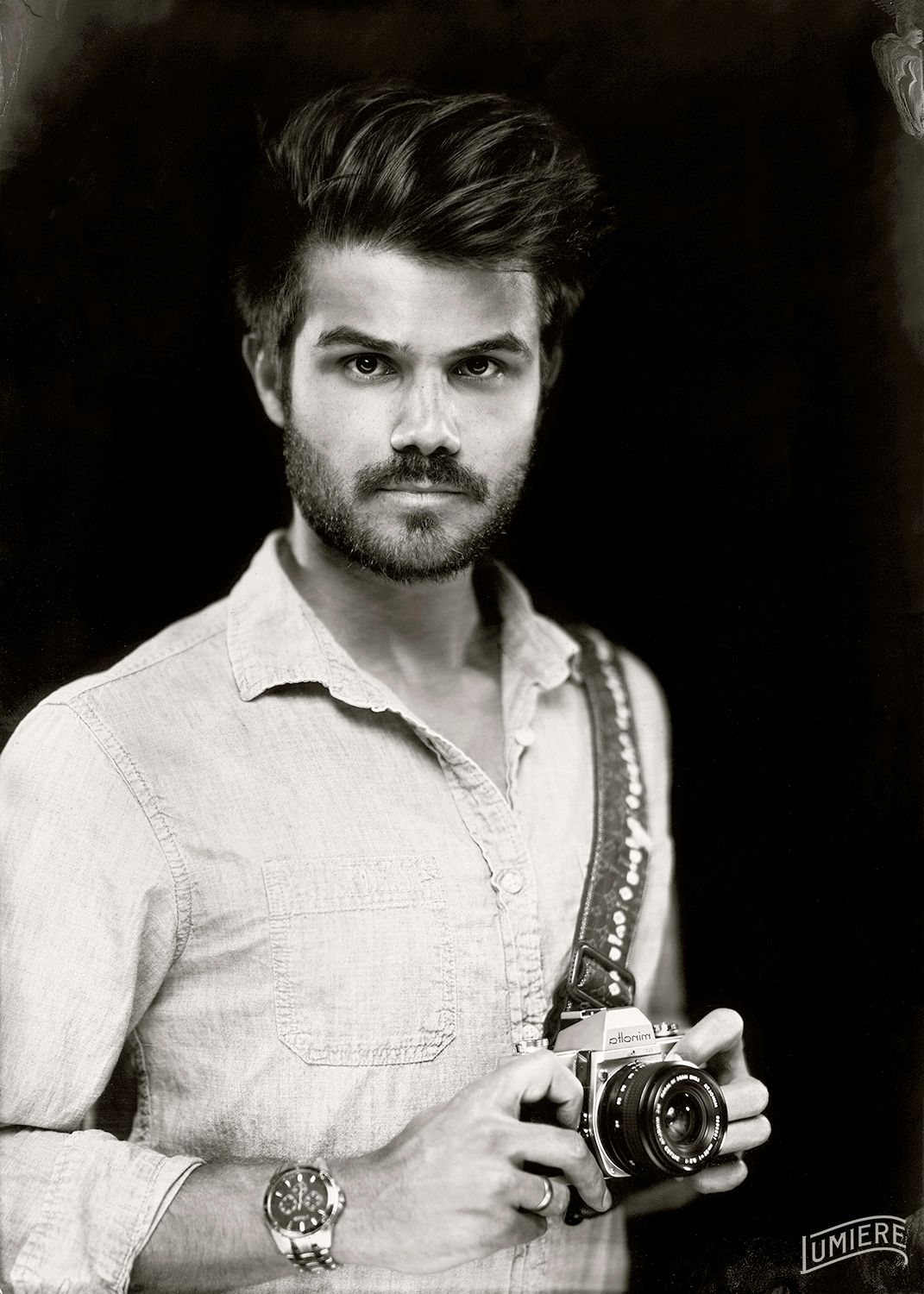 Vintage black and white portrait of a stylish bearded man holding a retro film camera confidently.