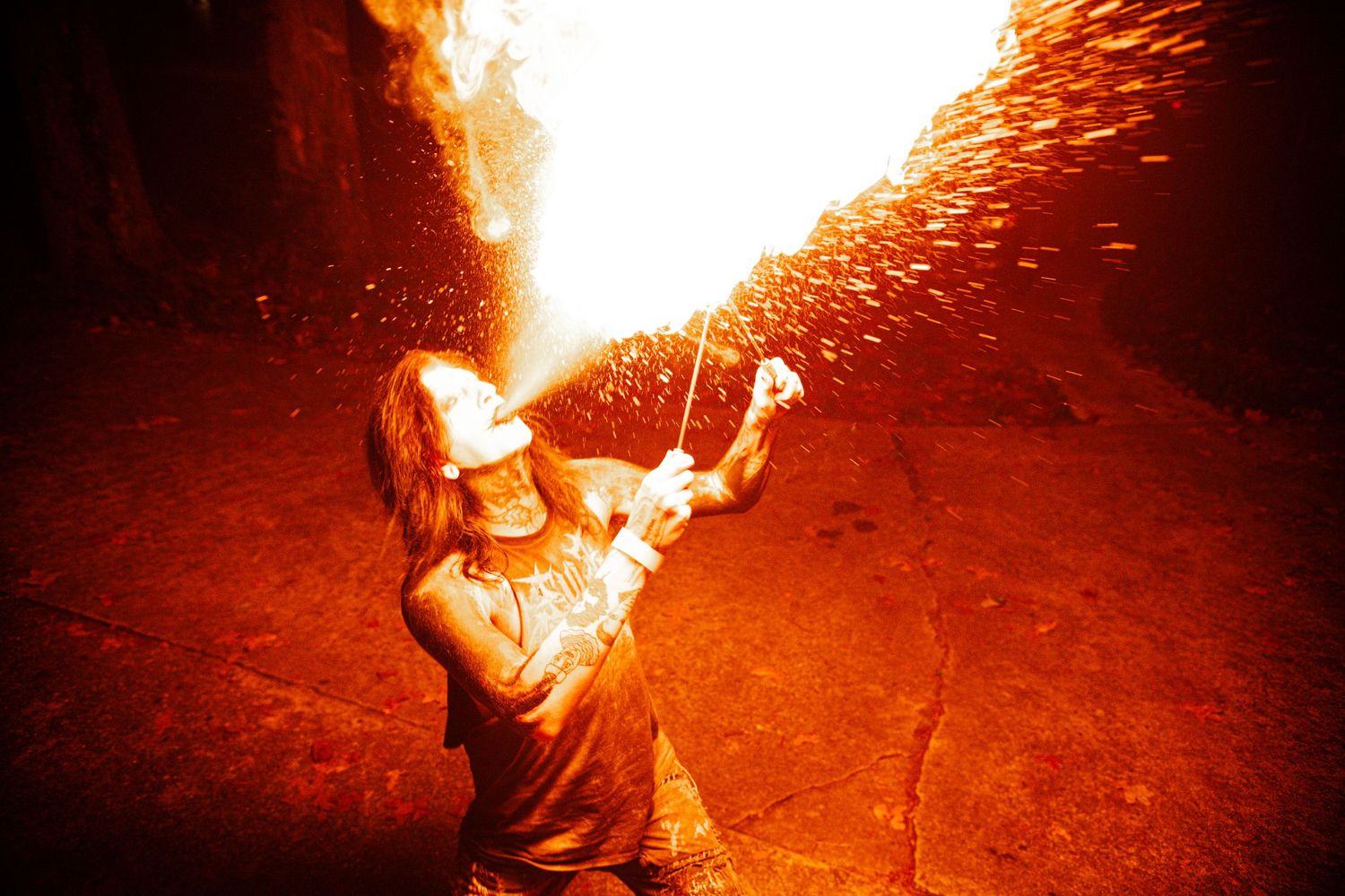 Person breathes fire in dramatic nighttime performance with glowing sparks.