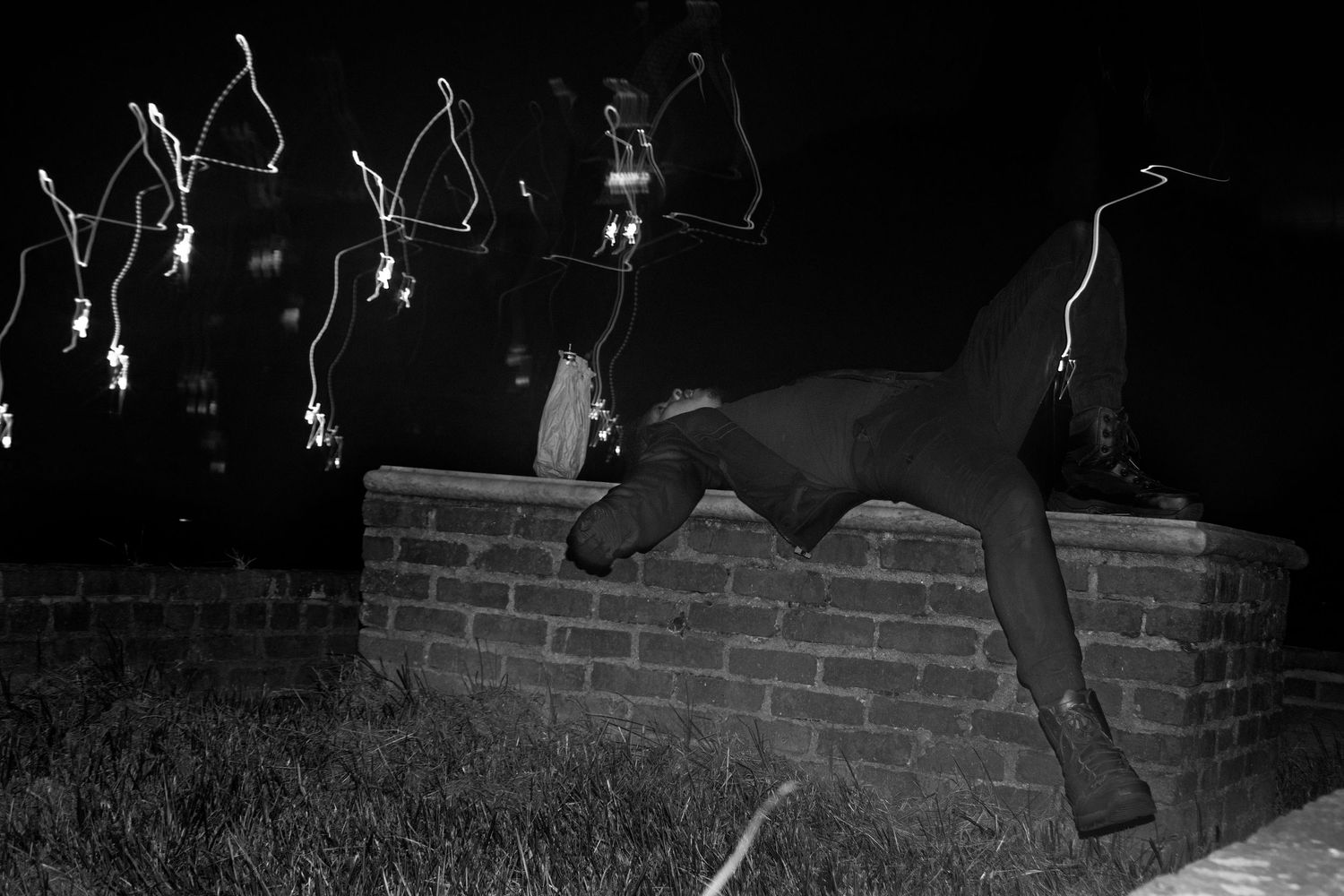 Black and white photo of a person vaulting over a brick wall at night.