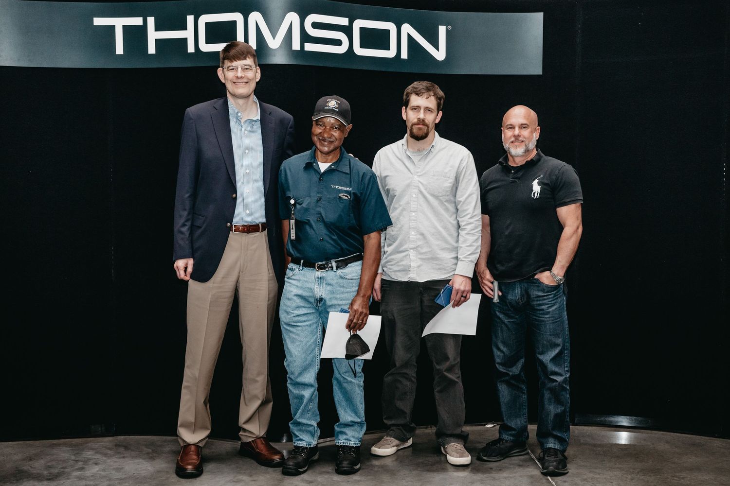 Four men posing together in front of a Thomson branded backdrop at a professional event.