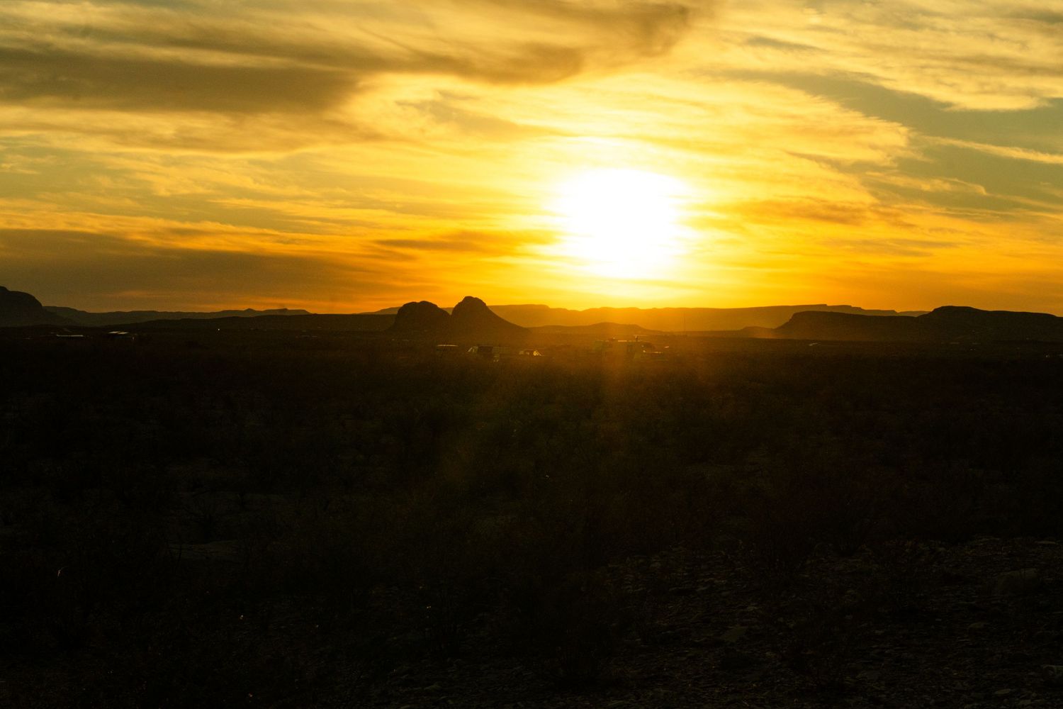 Golden sunset over silhouetted desert mountains with vibrant orange sky and dramatic clouds in an arid landscape.