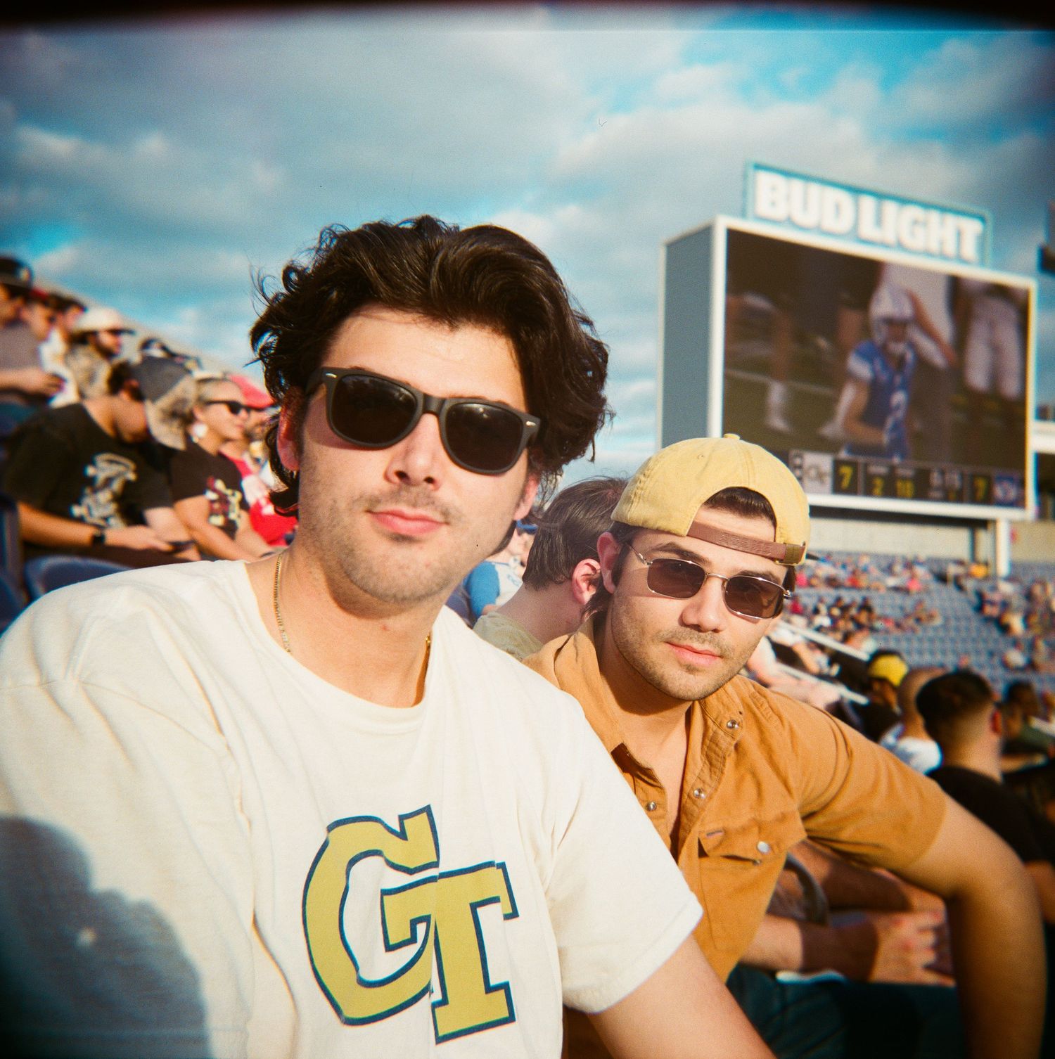 Two young men wearing sunglasses at Georgia Tech football game with Bud Light sign behind them.