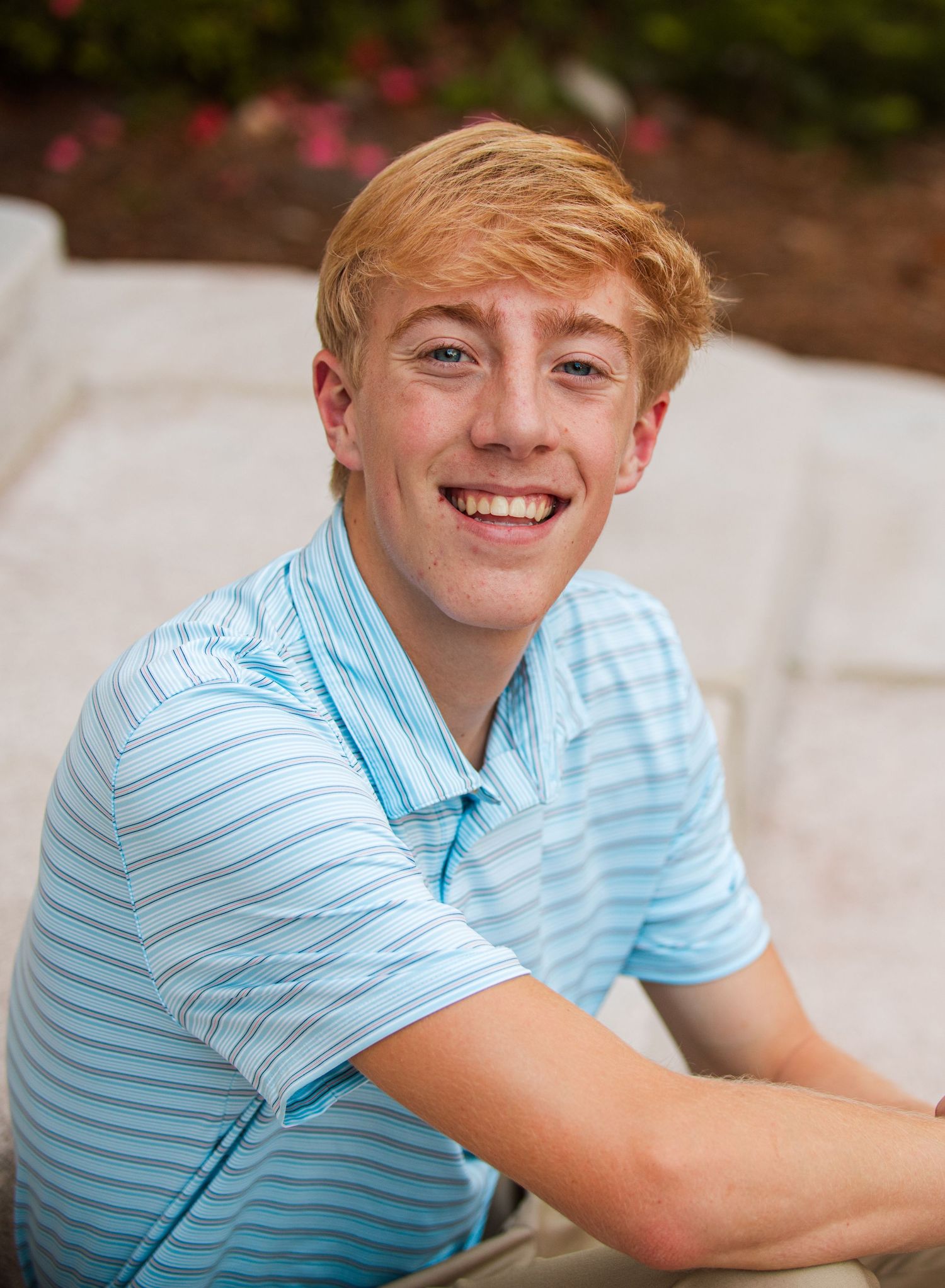 Smiling red-haired teen boy in a light blue striped polo sits outdoors on steps.