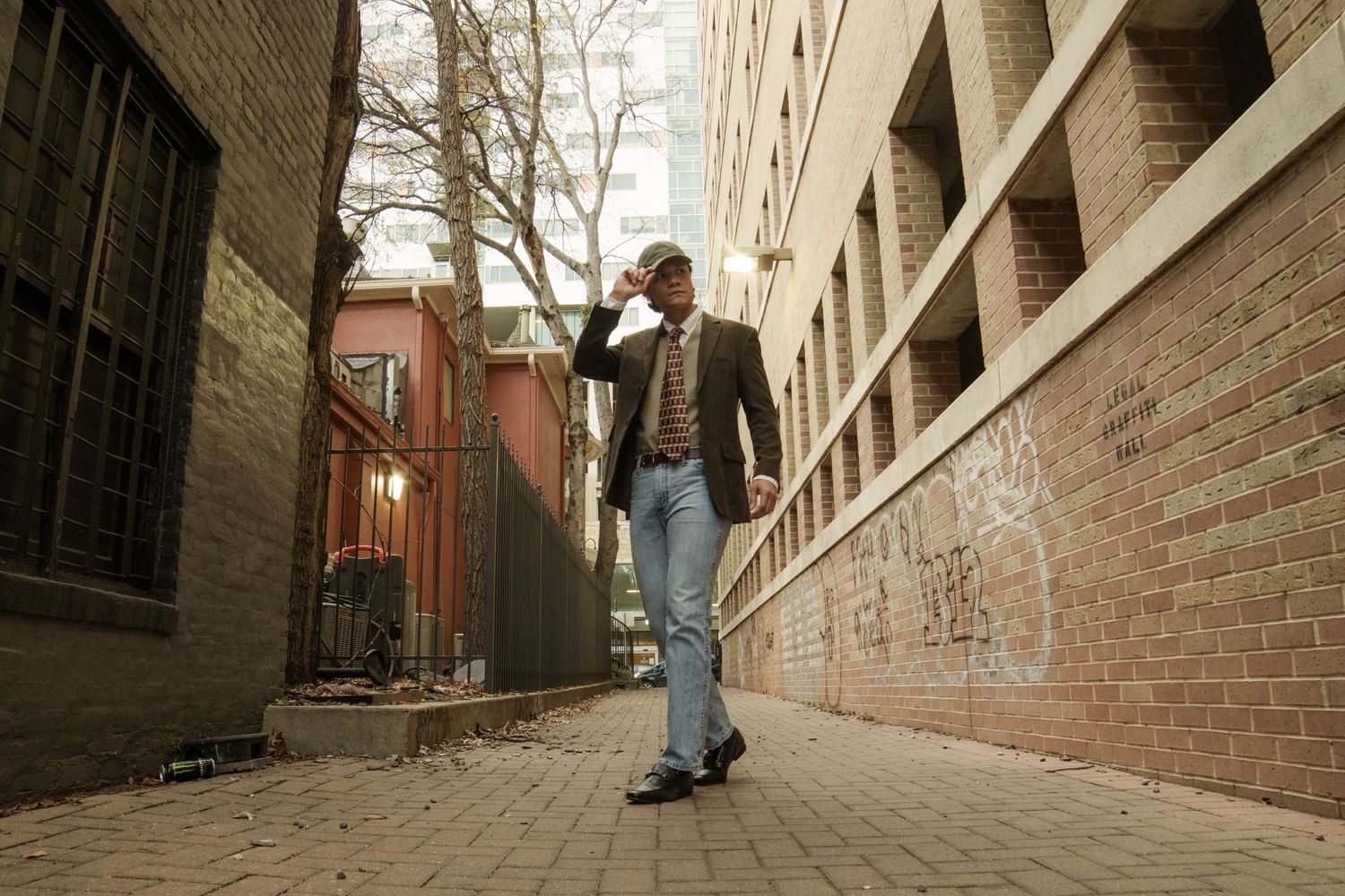 Documentary-style portrait of a stylish man in a blazer walking through a graffiti-lined urban alleyway, Austin street photography.