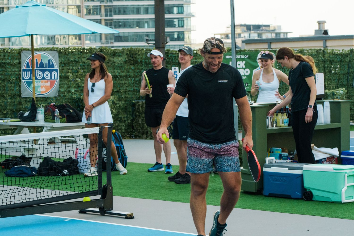 Players enjoy a rooftop pickleball game at Urban venue, with spectators watching on a sunny day.