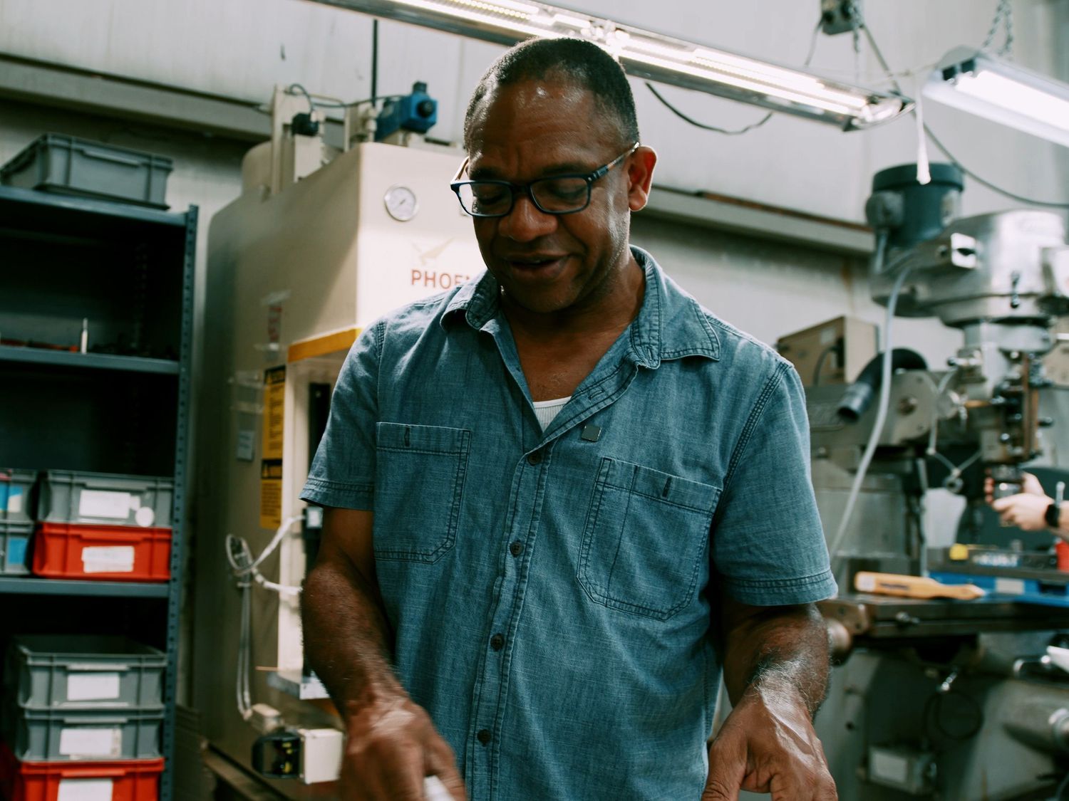 Skilled worker in denim shirt examines finished part in industrial machine shop environment.