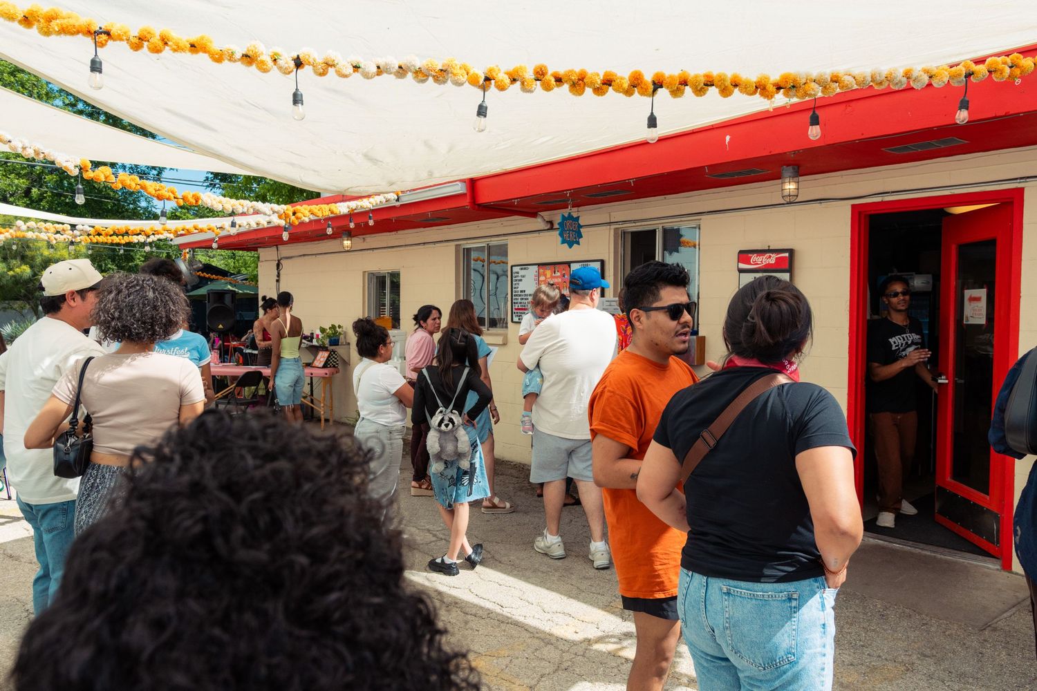 Crowd of people waiting in line outside a festive red building decorated with marigold garlands.