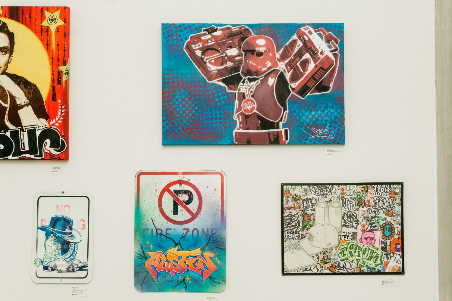 Street art gallery wall displaying graffiti-style paintings including a robot, no parking sign, and colorful murals.