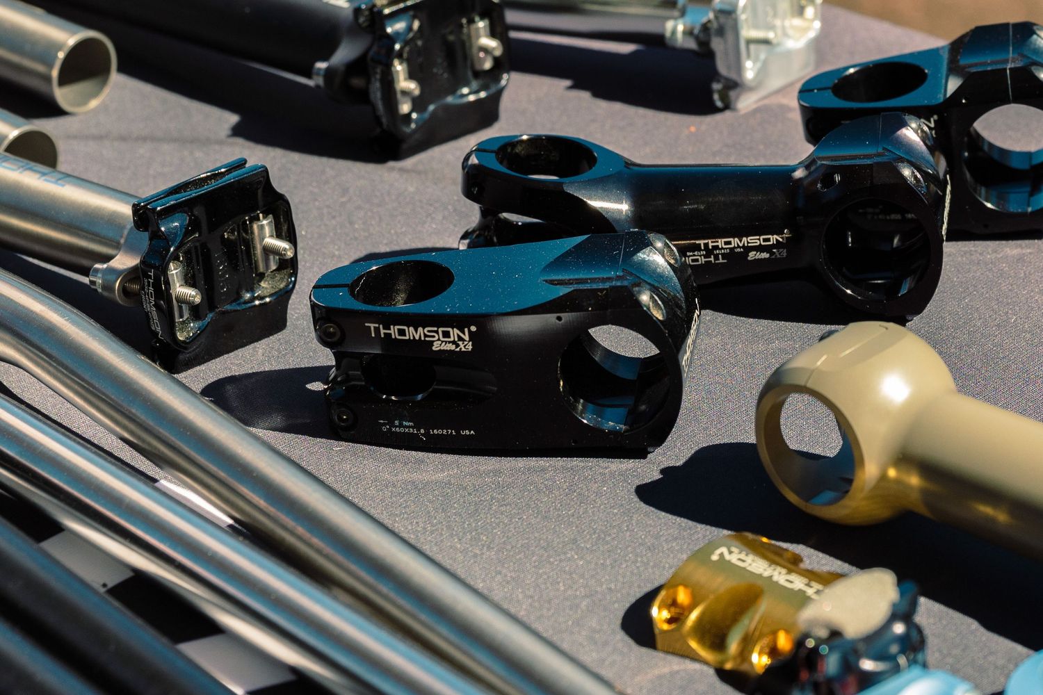 Black Thomson branded bicycle stems and components arranged on a sunlit table at an outdoor expo.