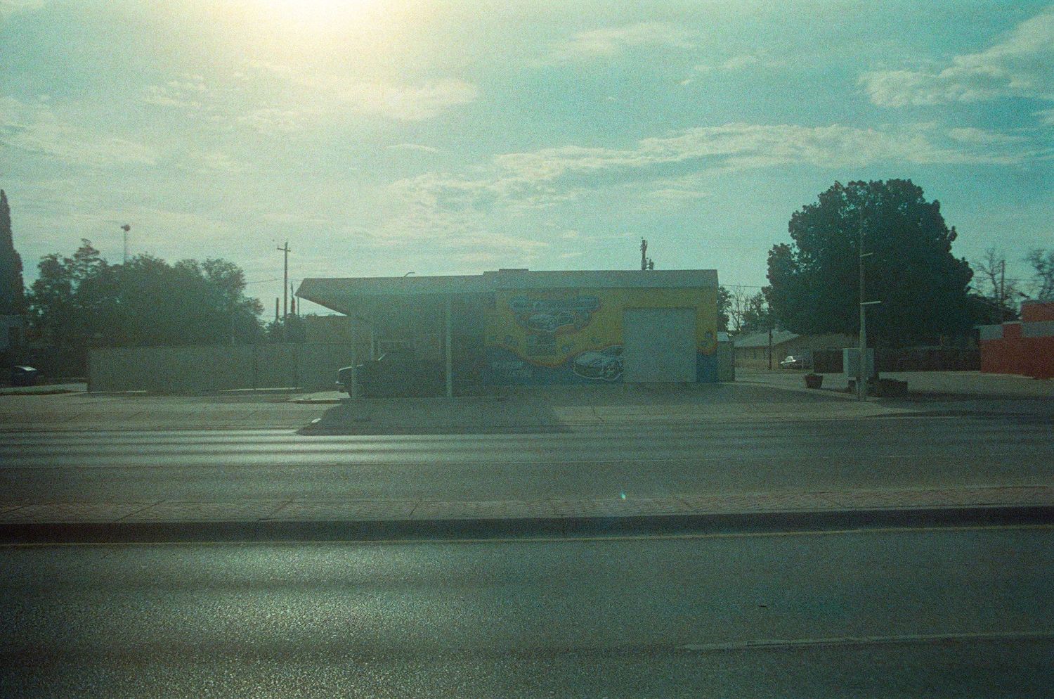 A roadside commercial building with a colorful mural on its facade, situated along a wide empty street under a bright sky.