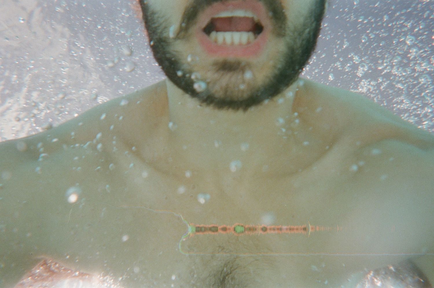 Man with beard submerged underwater, shirtless, with bubbles surrounding him in a dreamy aquatic scene.