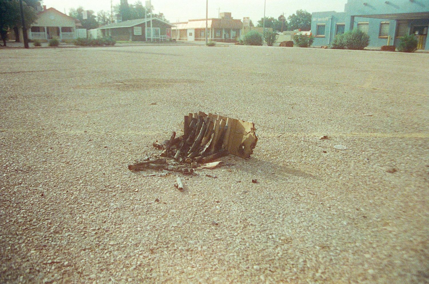 Burnt debris remnant on an empty asphalt parking lot with colorful buildings in the background.