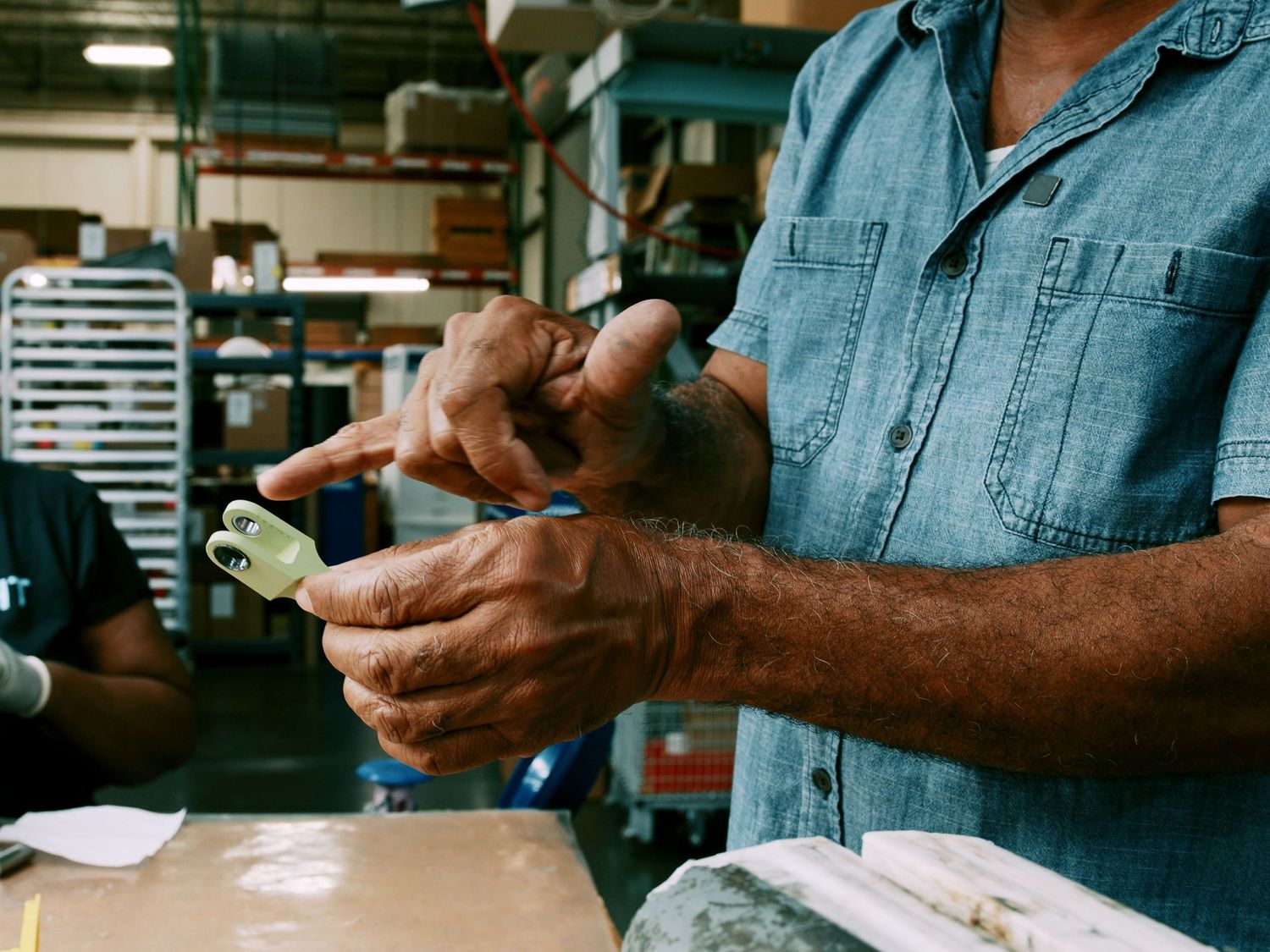 Worker inspects a small green machined component in a manufacturing facility.