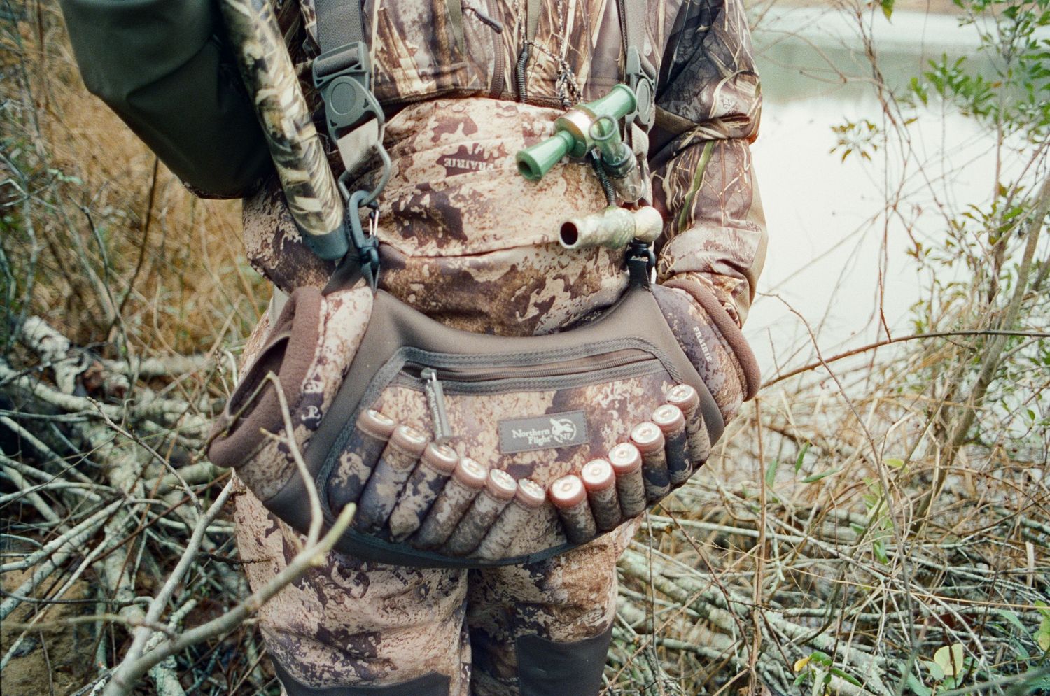 Close-up of a hunter in camouflage holding multiple shotgun shells in gloved hands outdoors.