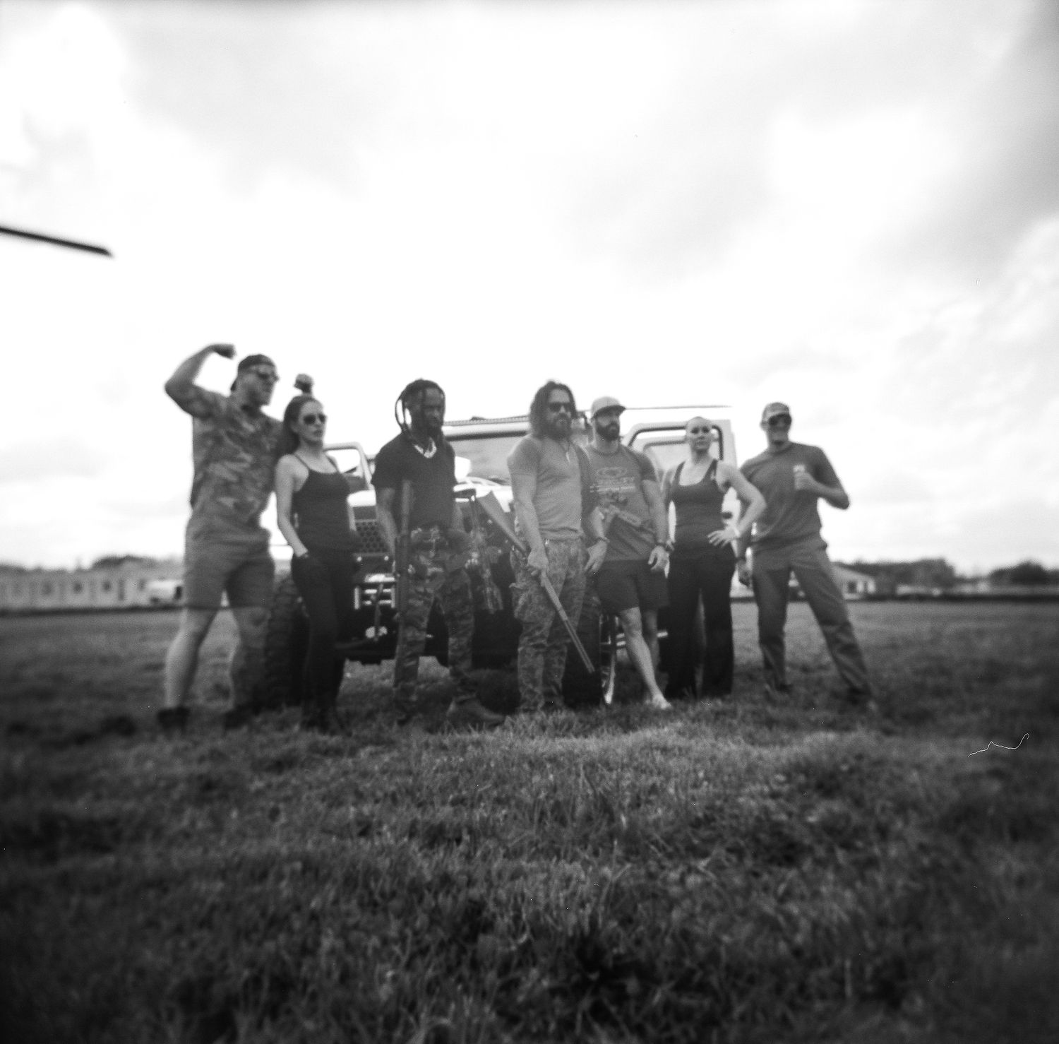 A group of people pose in front of a vehicle on a grass field in black and white photography.