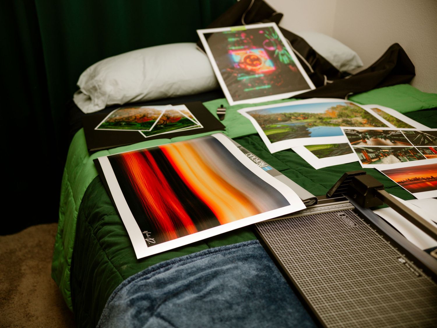 Collection of fine art landscape and abstract prints spread across a green bedspread.