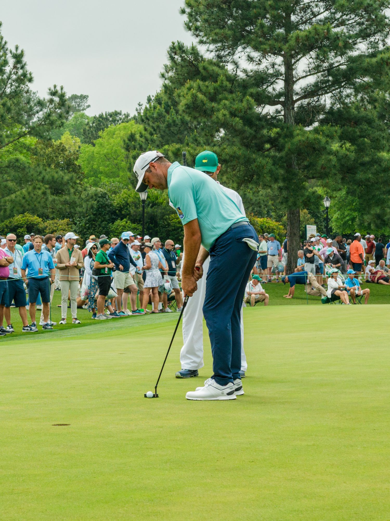 Golfer putting on a green at Augusta National during The Masters tournament with spectators watching.
