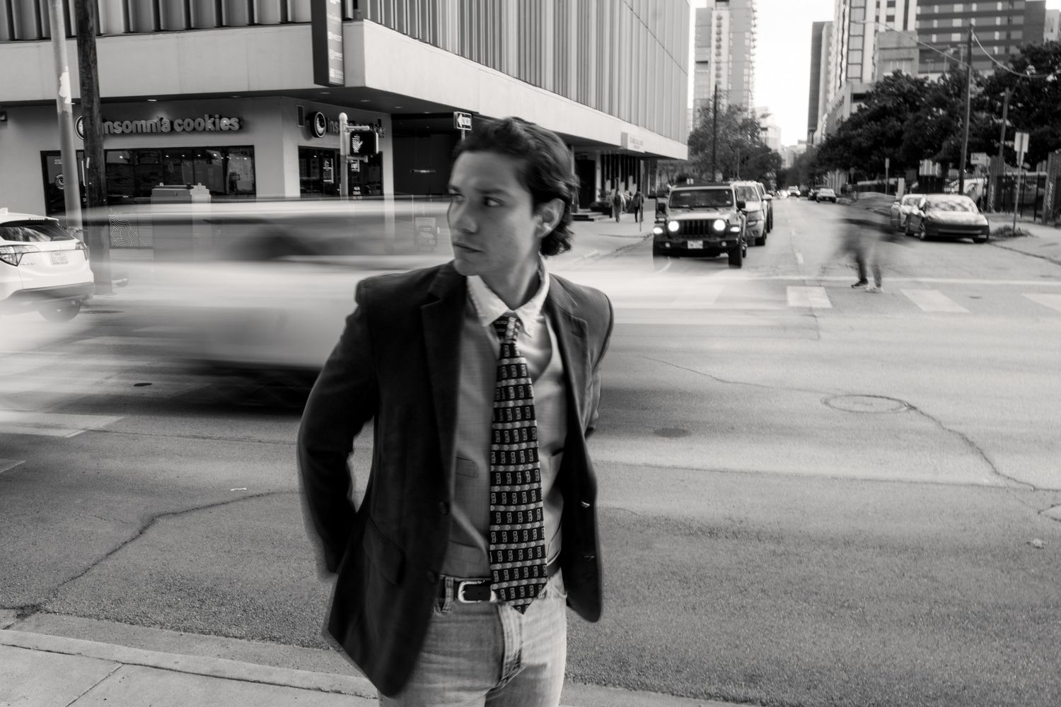 Black and white photo of man in suit and tie standing on busy city street.