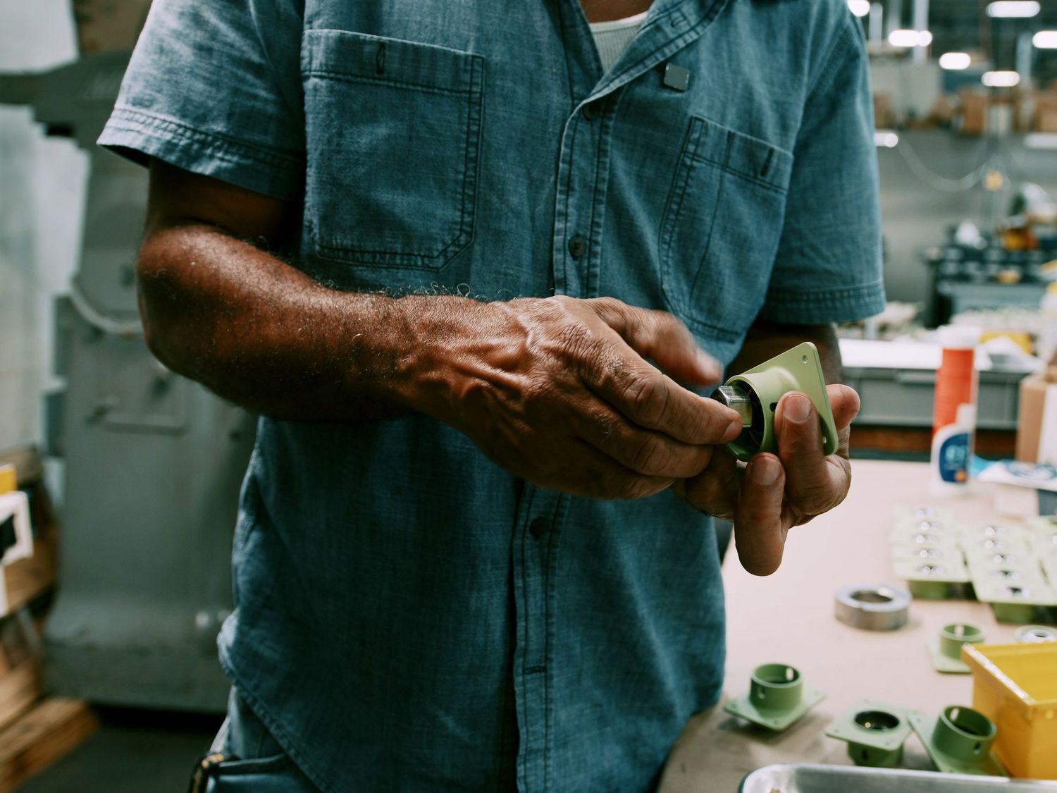 Craftsman in denim shirt carefully inspects small green ceramic piece in workshop setting.