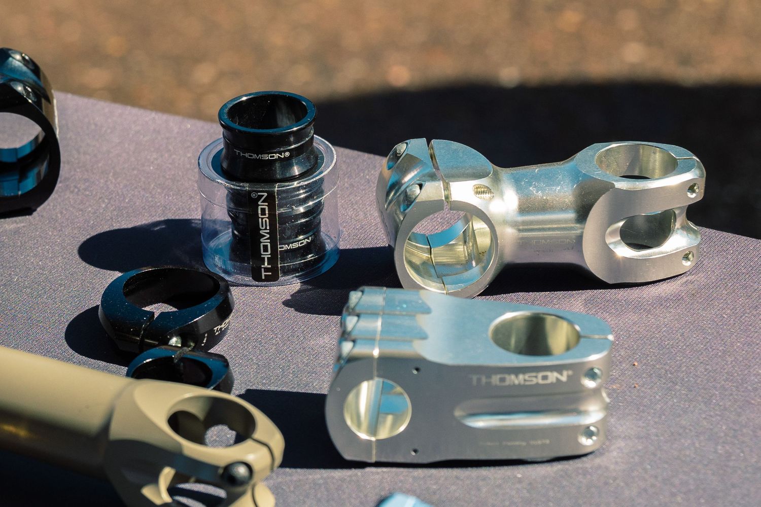 Thomson branded silver and black bicycle stems and headset components displayed on a table outdoors.