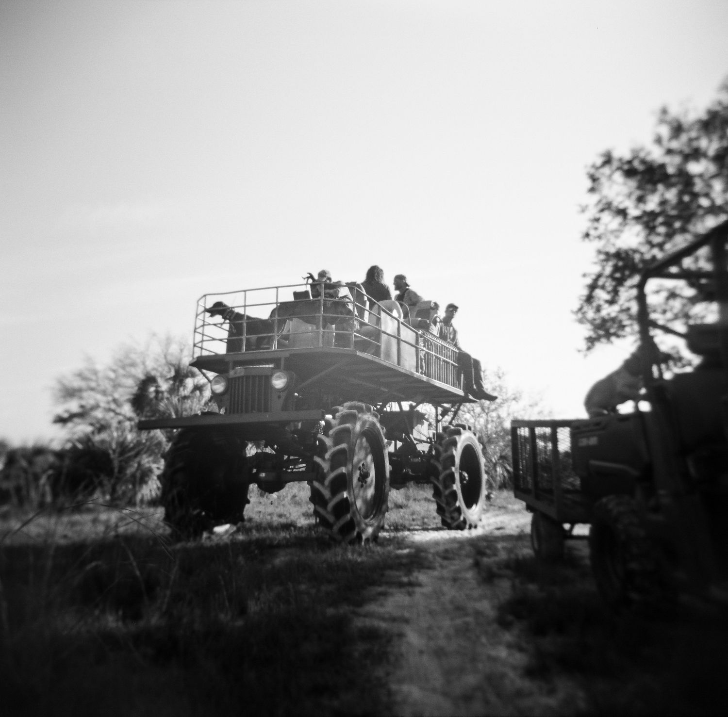 Black and white photo of a large off-road vehicle carrying passengers through open wilderness terrain.