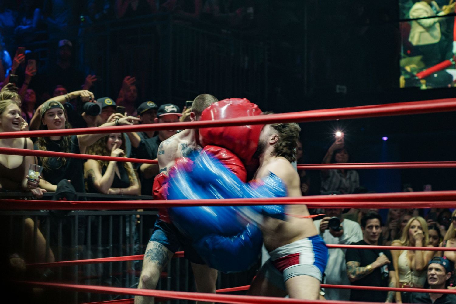 Two boxers clash in a wrestling ring surrounded by an excited crowd at a live boxing event.