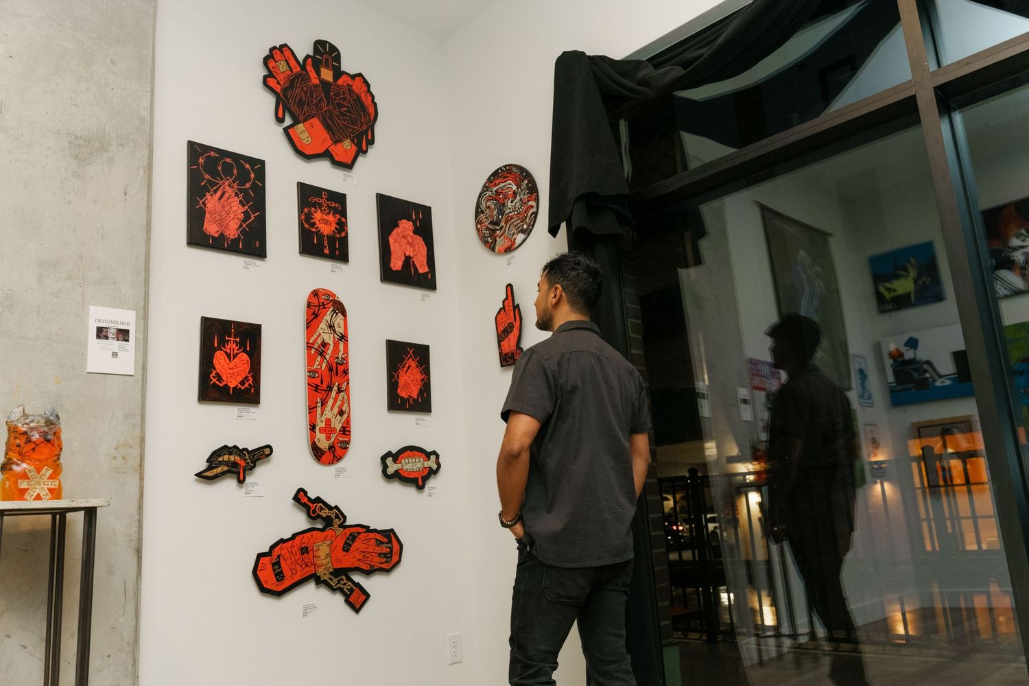 Visitor views red and black pixel art pieces displayed on white gallery wall at night.
