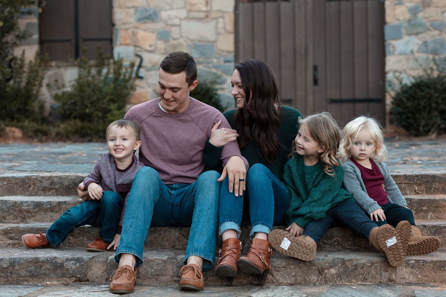 Family of five laughing together while sitting on stone steps in casual attire.